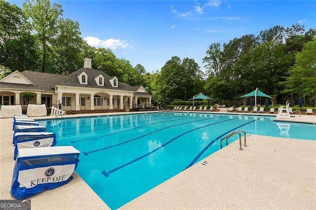 community pool with view of wooded area and a patio area