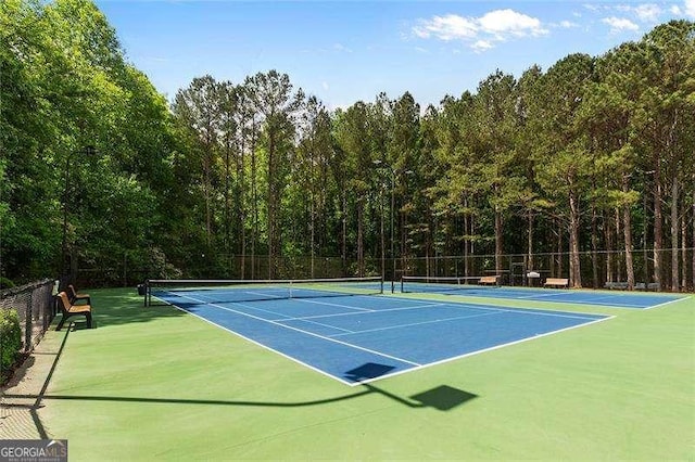 view of tennis court featuring fence and a wooded view