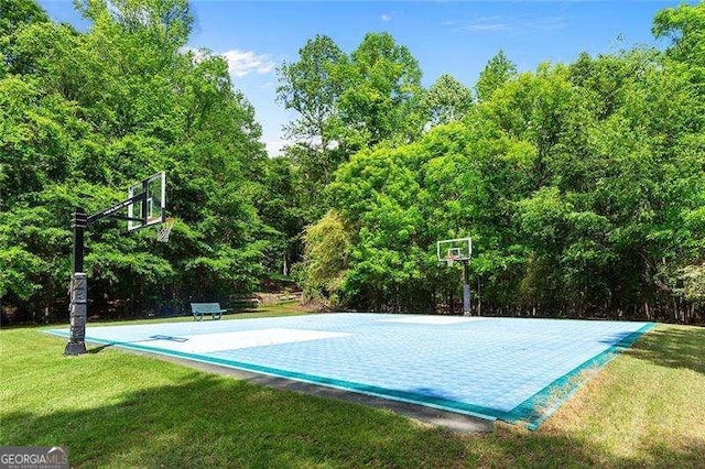 view of basketball court with a yard, basketball court, and a wooded view