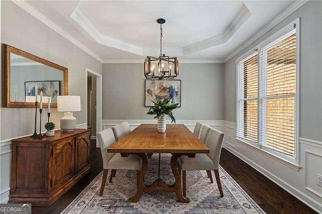 dining room featuring dark wood-style flooring, a chandelier, a raised ceiling, a decorative wall, and a wainscoted wall