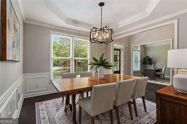 dining area featuring healthy amount of natural light, a chandelier, ornamental molding, a raised ceiling, and a decorative wall