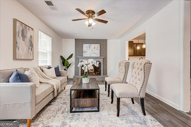 living room with wood finished floors, ceiling fan, baseboards, a brick fireplace, and a textured ceiling