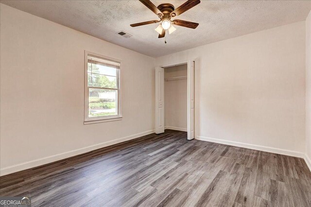 unfurnished bedroom with wood finished floors, a textured ceiling, baseboards, and a closet