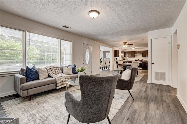 living area with light wood-style flooring, a textured ceiling, baseboards, and a ceiling fan