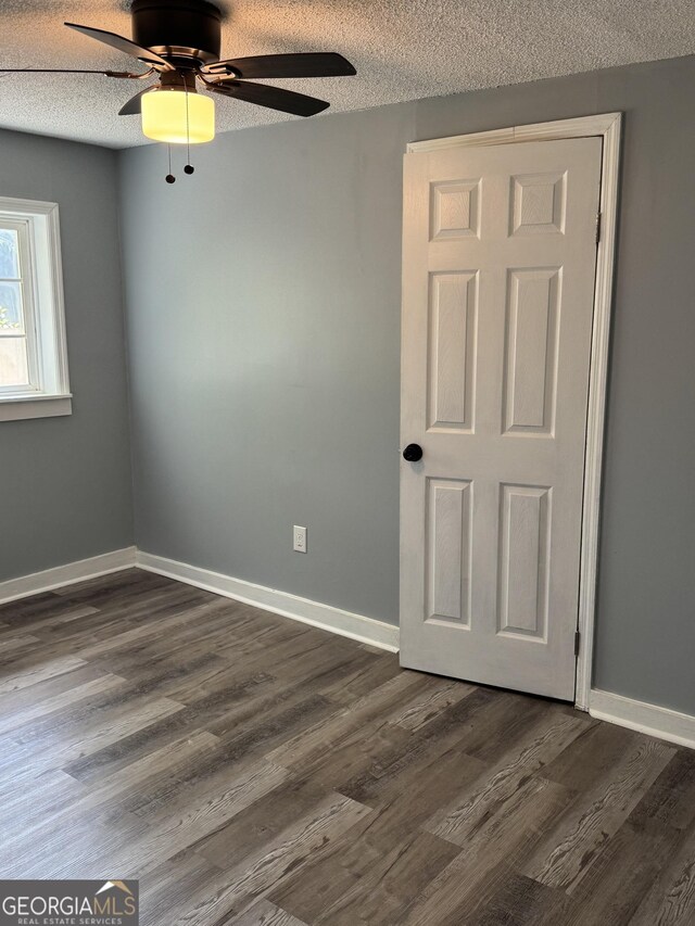 spare room with a textured ceiling, dark wood-style floors, ceiling fan, and baseboards
