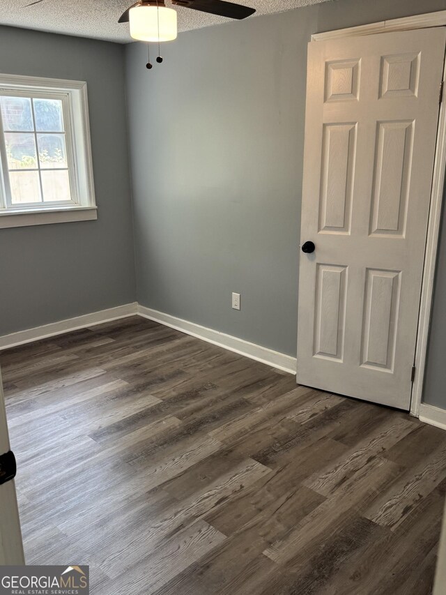 unfurnished room featuring a ceiling fan, a textured ceiling, dark wood-style flooring, and baseboards