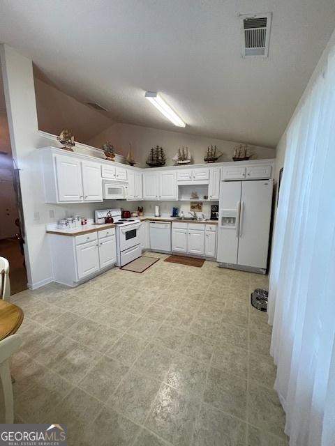 kitchen with white appliances, vaulted ceiling, white cabinetry, a sink, and light countertops
