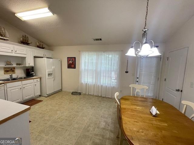 kitchen featuring white refrigerator with ice dispenser, a sink, vaulted ceiling, a chandelier, and white cabinets