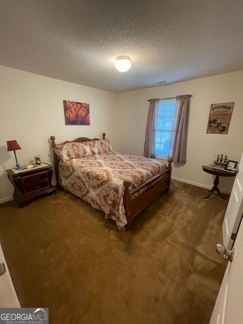 bedroom with a textured ceiling, dark carpet, and baseboards