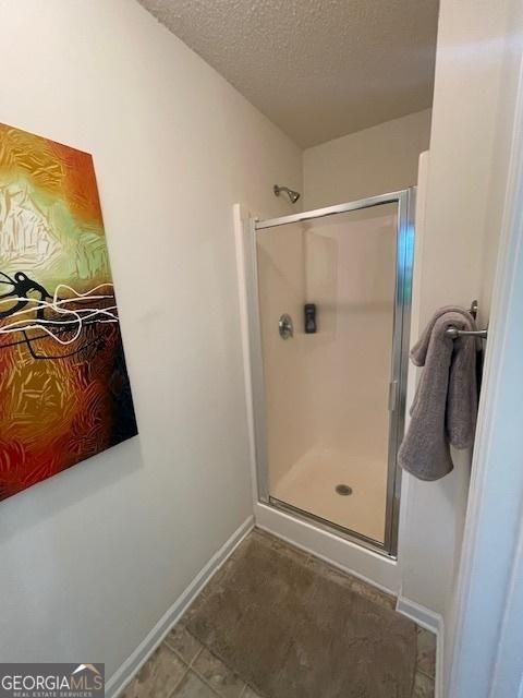 full bath with a shower stall, baseboards, and a textured ceiling