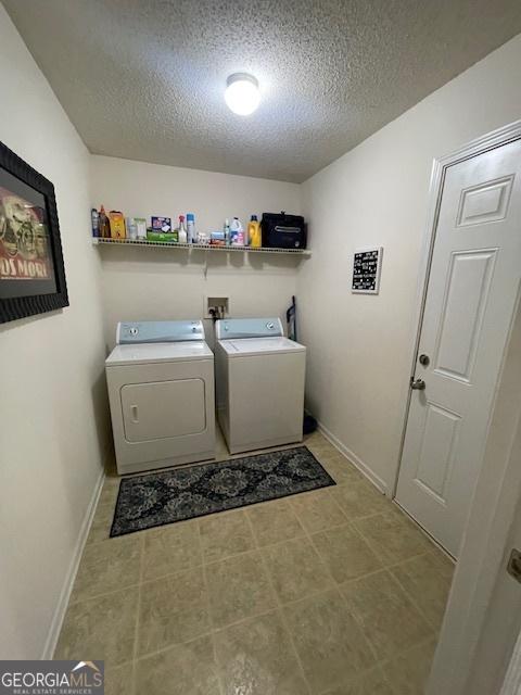 clothes washing area featuring washing machine and dryer, a textured ceiling, and baseboards