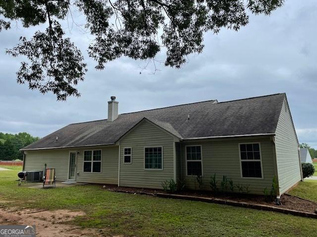 back of property featuring a chimney, a lawn, a shingled roof, and central AC unit