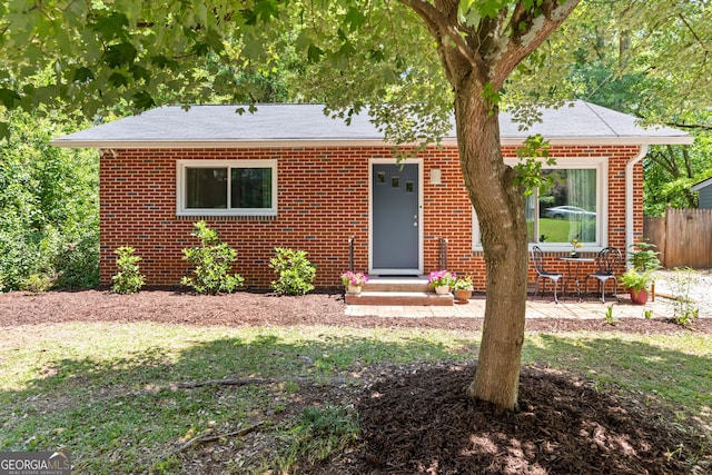 view of front facade with brick siding, fence, and roof with shingles