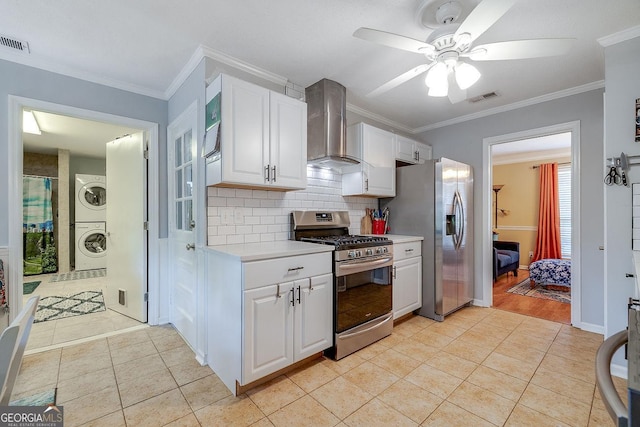 kitchen featuring stainless steel appliances, stacked washer and clothes dryer, wall chimney exhaust hood, a ceiling fan, and light tile patterned floors