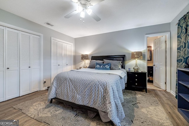 bedroom featuring wood finished floors, two closets, ceiling fan, baseboards, and ensuite bath