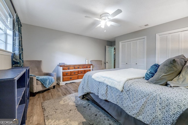 bedroom with two closets, wood finished floors, and a ceiling fan