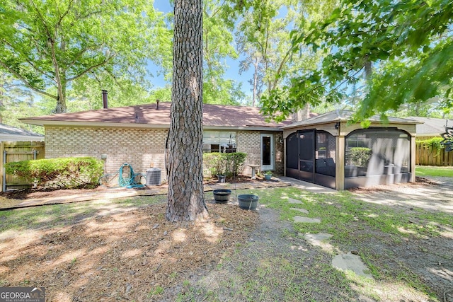 rear view of house with a sunroom, brick siding, fence, and central AC