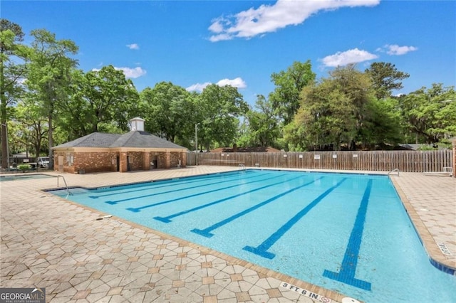 community pool with fence, view of scattered trees, and a patio area