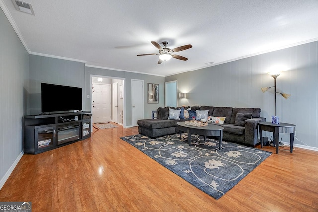 living area with wood finished floors, crown molding, ceiling fan, and baseboards