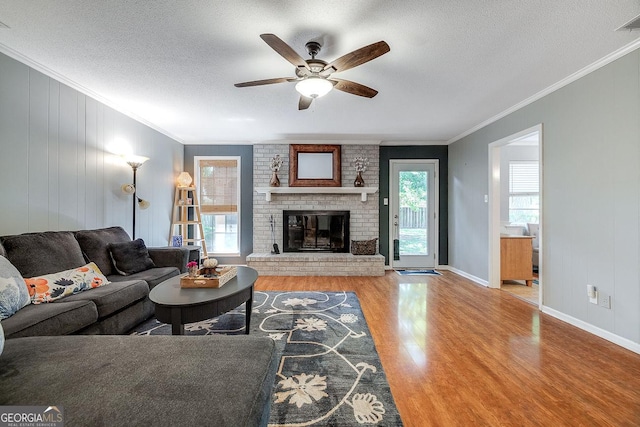 living room featuring wood finished floors, crown molding, a ceiling fan, a textured ceiling, and a brick fireplace