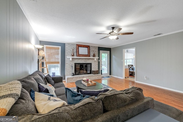 living room featuring wood finished floors, ornamental molding, ceiling fan, a fireplace, and baseboards