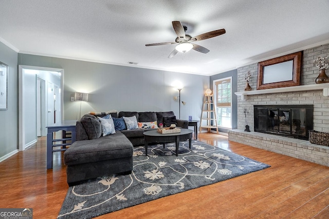 living room with crown molding, wood finished floors, a ceiling fan, a fireplace, and a textured ceiling