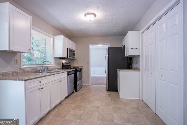 1076 Plantation Blvd SE, Conyers, GA 30094 - kitchen with appliances with stainless steel finishes, a sink, white cabinets, a textured ceiling, and baseboards