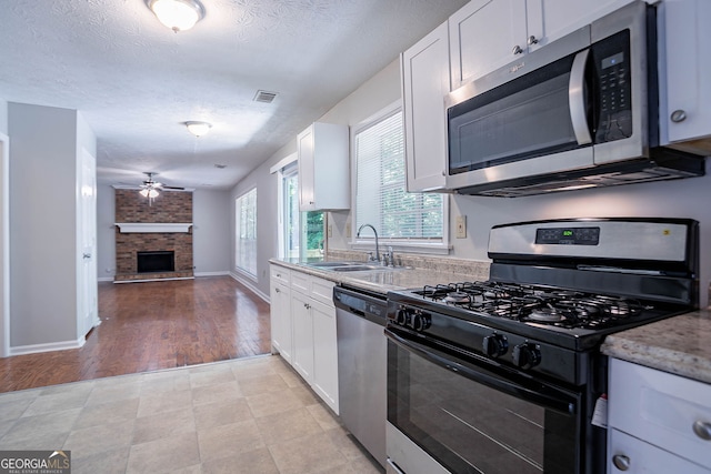 1076 Plantation Blvd SE, Conyers, GA 30094 - kitchen featuring stainless steel appliances, a large fireplace, ceiling fan, white cabinets, and a textured ceiling