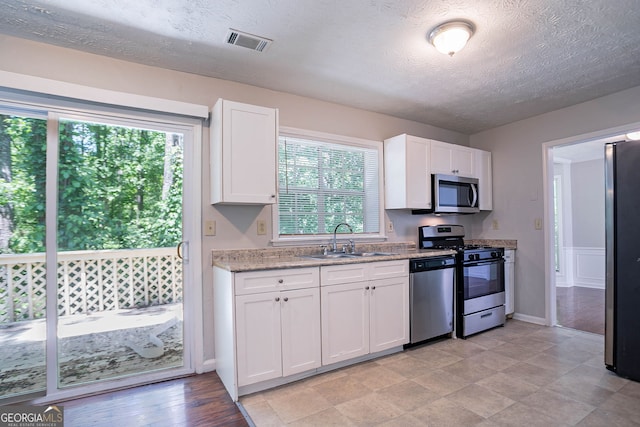 1076 Plantation Blvd SE, Conyers, GA 30094 - kitchen featuring appliances with stainless steel finishes, healthy amount of natural light, white cabinets, a textured ceiling, and light stone counters