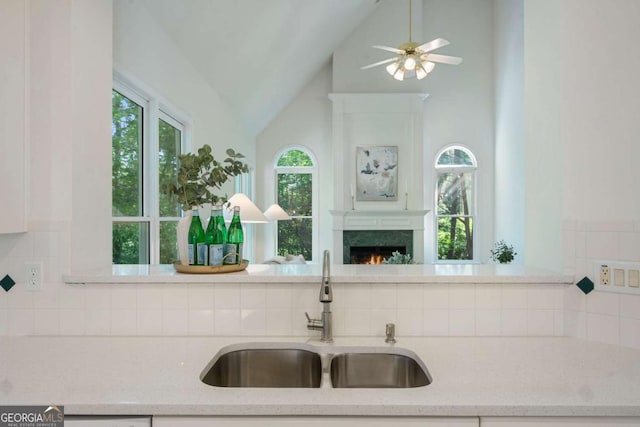 kitchen featuring a sink, a lit fireplace, tasteful backsplash, vaulted ceiling, and light stone countertops