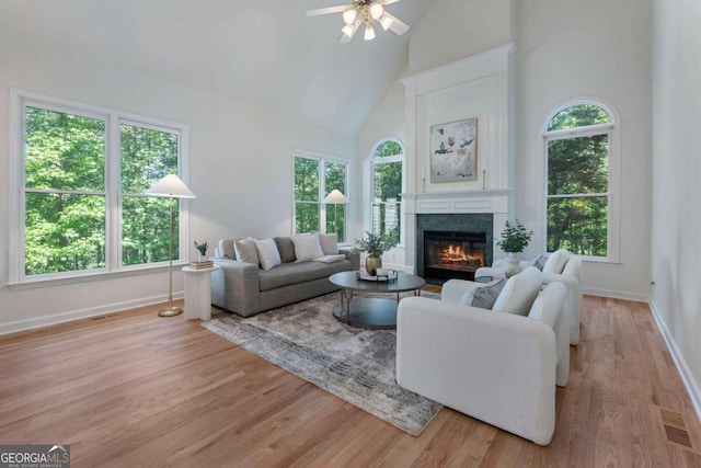 living area featuring high vaulted ceiling, ceiling fan, a glass covered fireplace, baseboards, and light wood-style flooring