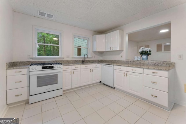 kitchen with white appliances, white cabinets, a sink, light stone counters, and light tile patterned floors