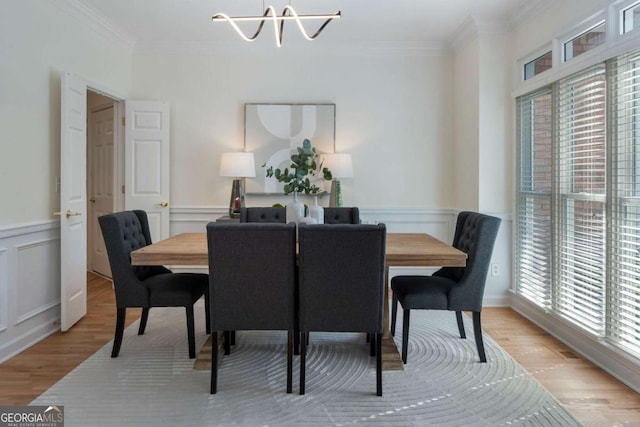 dining area featuring a chandelier, ornamental molding, light wood-style floors, a decorative wall, and wainscoting