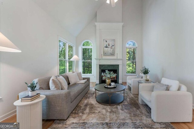 living area featuring high vaulted ceiling, wood finished floors, a fireplace, a ceiling fan, and baseboards
