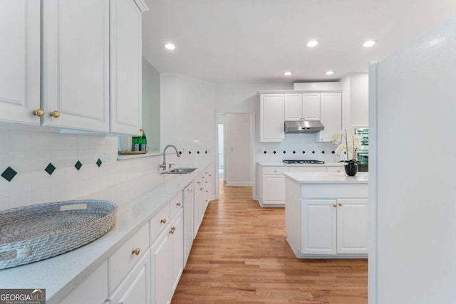 kitchen featuring under cabinet range hood, a sink, decorative backsplash, light wood-style flooring, and white cabinets