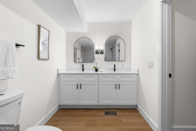 full bathroom with toilet, wood finished floors, double vanity, and baseboards