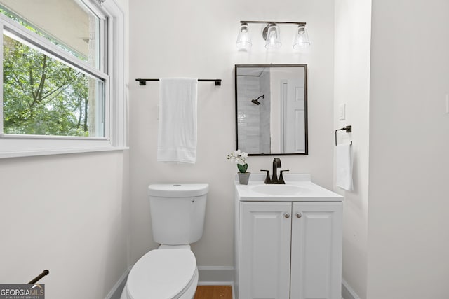 full bath featuring toilet, tiled shower, vanity, and baseboards