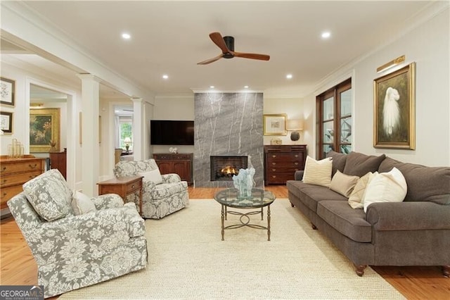 living area featuring ornamental molding, a ceiling fan, a fireplace, decorative columns, and light wood finished floors