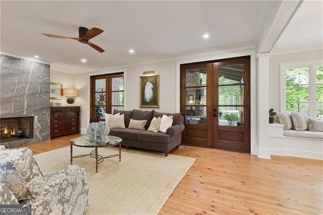 living room with crown molding, wood finished floors, ceiling fan, a large fireplace, and french doors