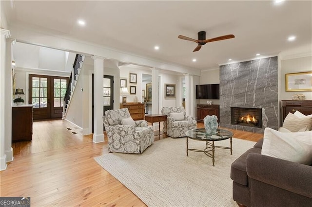 living room featuring ceiling fan, a high end fireplace, light wood-style flooring, ornamental molding, and ornate columns