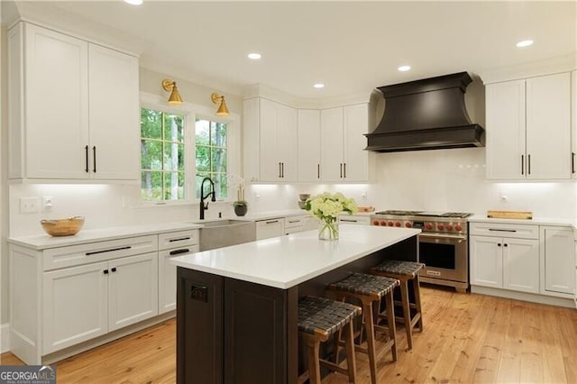 kitchen with custom range hood, high end stainless steel range oven, a kitchen bar, white cabinetry, and recessed lighting