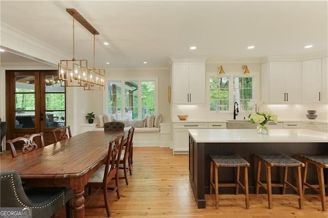 kitchen with a sink, white cabinets, crown molding, a kitchen breakfast bar, and light wood-style flooring