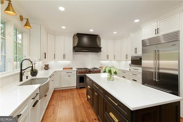 kitchen with custom exhaust hood, high end appliances, a sink, white cabinets, and recessed lighting