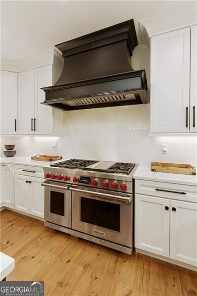 kitchen featuring range with two ovens, custom range hood, light countertops, white cabinetry, and light wood finished floors