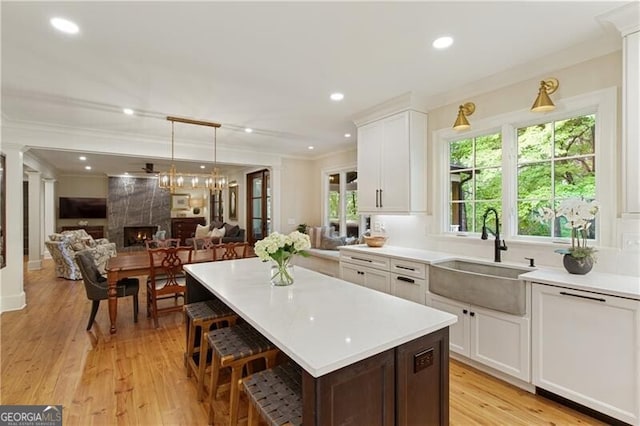 kitchen with a sink, ornamental molding, open floor plan, light countertops, and white cabinetry