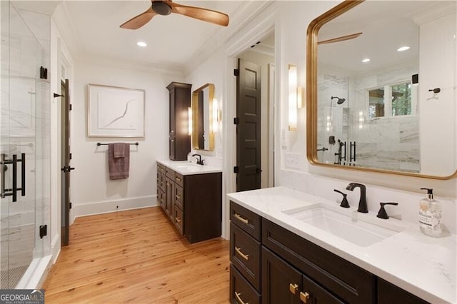 bathroom featuring a stall shower, wood finished floors, a ceiling fan, ornamental molding, and two vanities