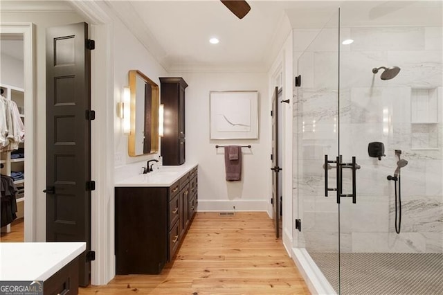 bathroom featuring wood finished floors, a shower stall, baseboards, vanity, and crown molding