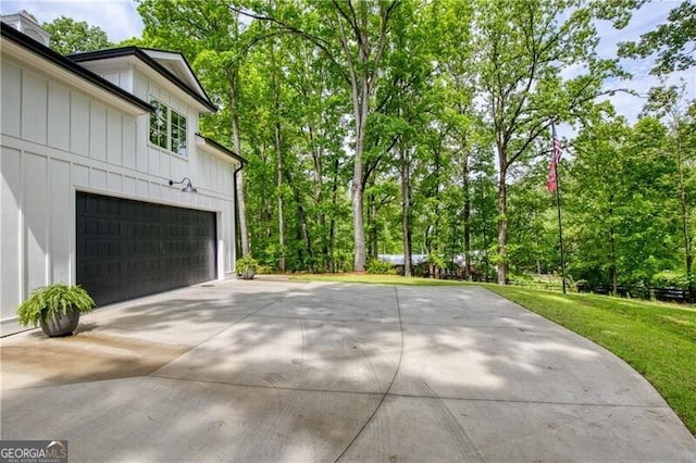 view of side of home with board and batten siding, an attached garage, view of wooded area, and a chimney