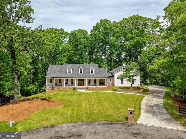 cape cod house with a porch, concrete driveway, a front lawn, and view of scattered trees