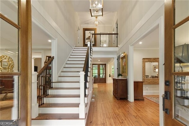 foyer entrance with stairway, wood finished floors, crown molding, a towering ceiling, and french doors
